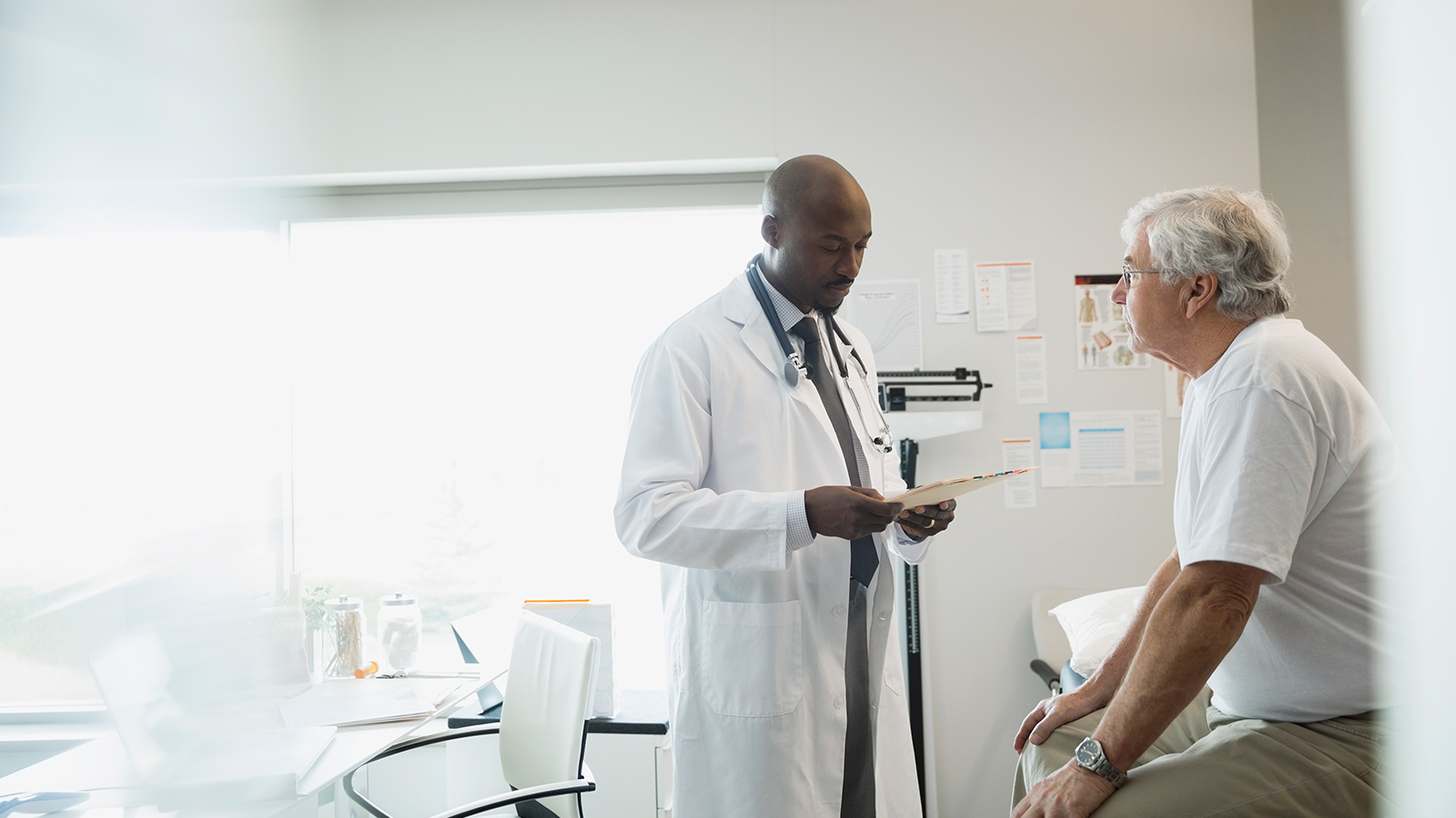 Doctor standing and speaking to a sitting patient in a hospital room.