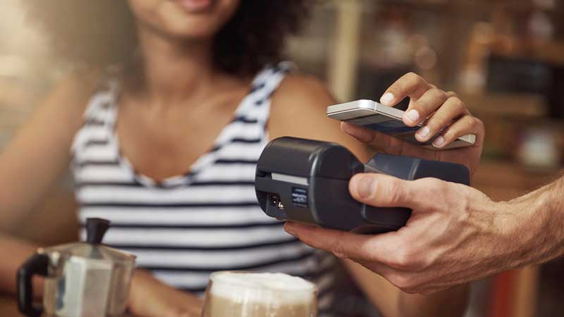 A woman at a café make a contactless payment on a card reader using her device.