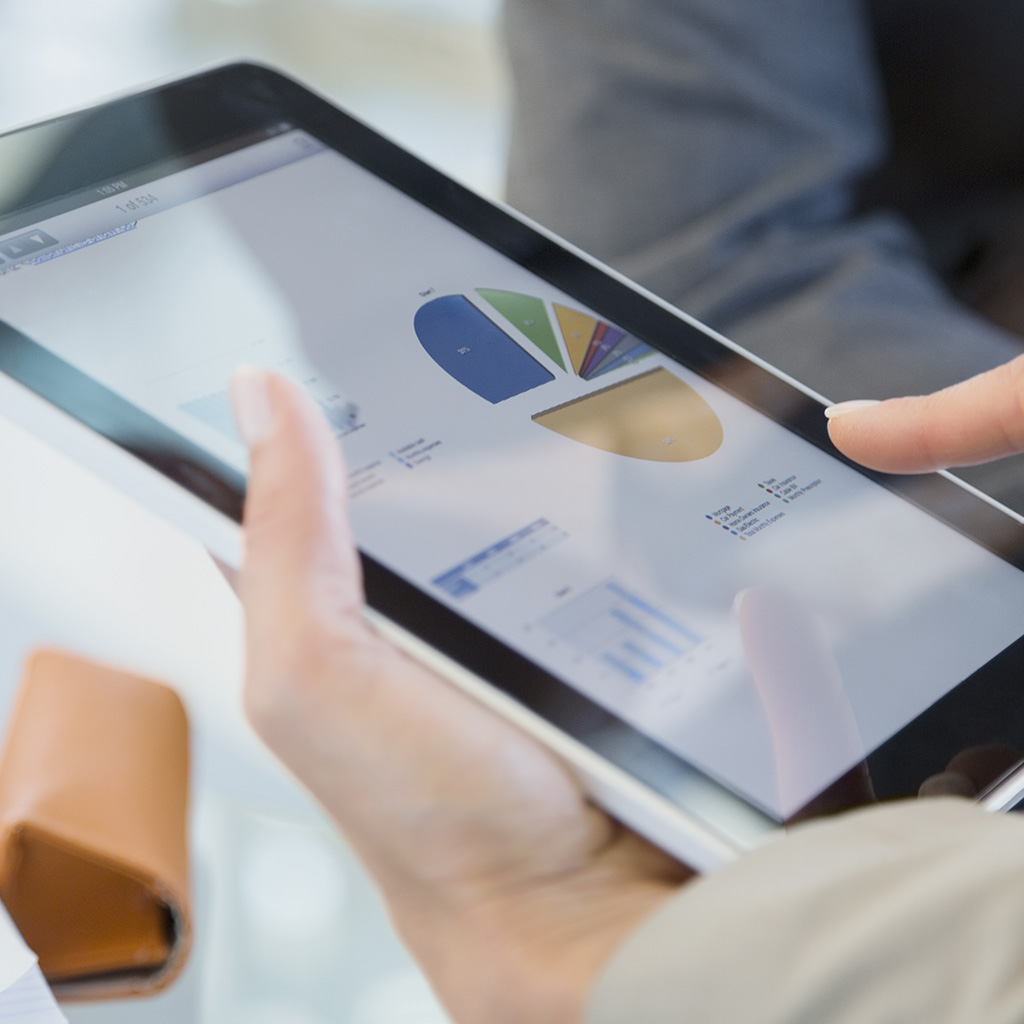 Person holding a tablet with graphs and a pie chart on the screen.