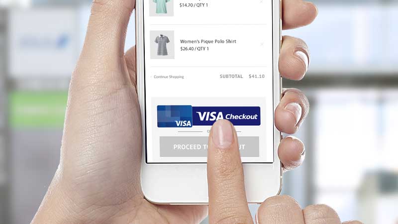 A hand holding a smart phone with the user's index finger clicking on a Visa Checkout button on a retailer website to complete the payment process.