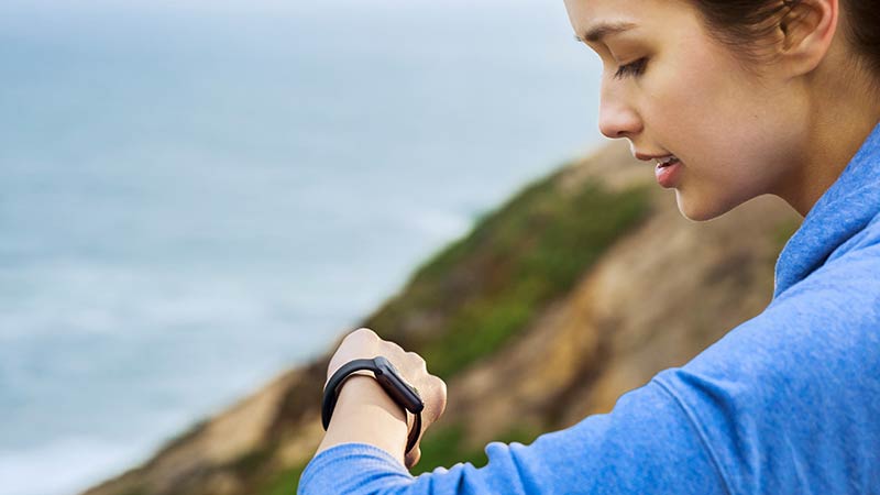 Woman checking her watch on top of a cliff overlooking the ocean.